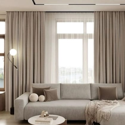Floor-length cream drapes with sheers behind them at a corner window in a living room.